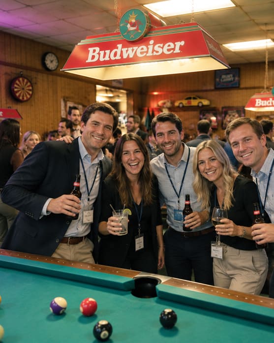 Friends smiling together at a pool table beneath a Budweiser lamp