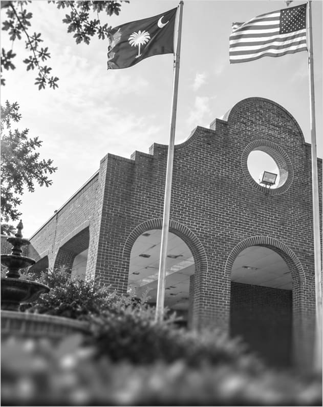 A brick building with arched openings and a round window, with the South Carolina and American flags flying beside it