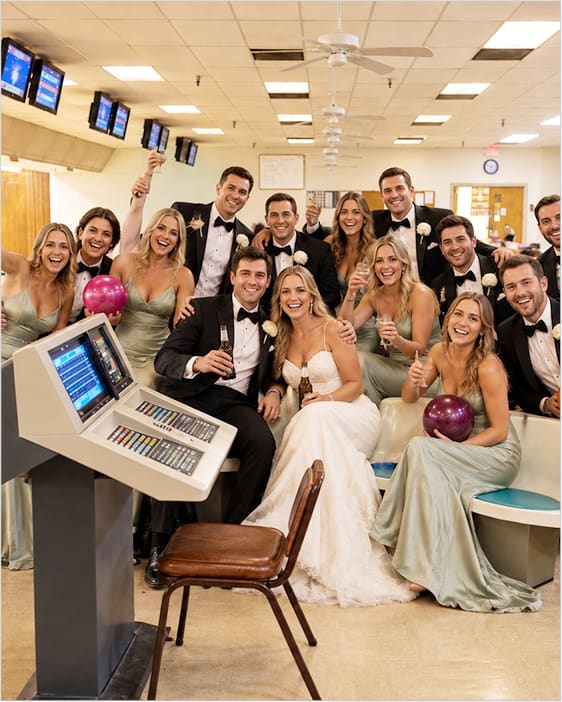 A wedding party in formalwear holding bowling balls and drinks, laughing together