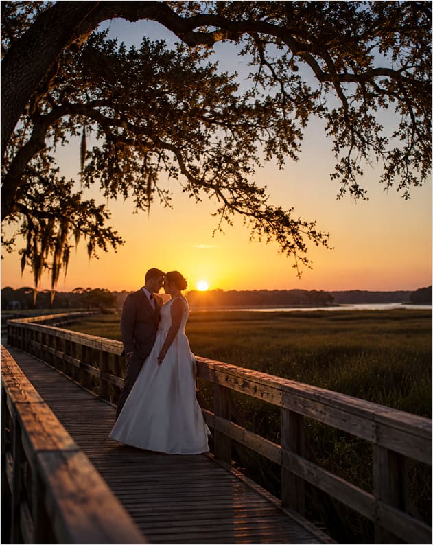 A couple embracing on a boardwalk over the marsh at sunset