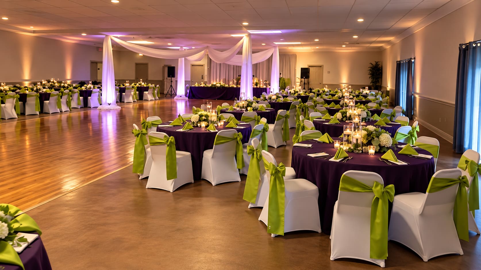 The hall set for a reception, with draped fabric, round tables and a wood dance floor